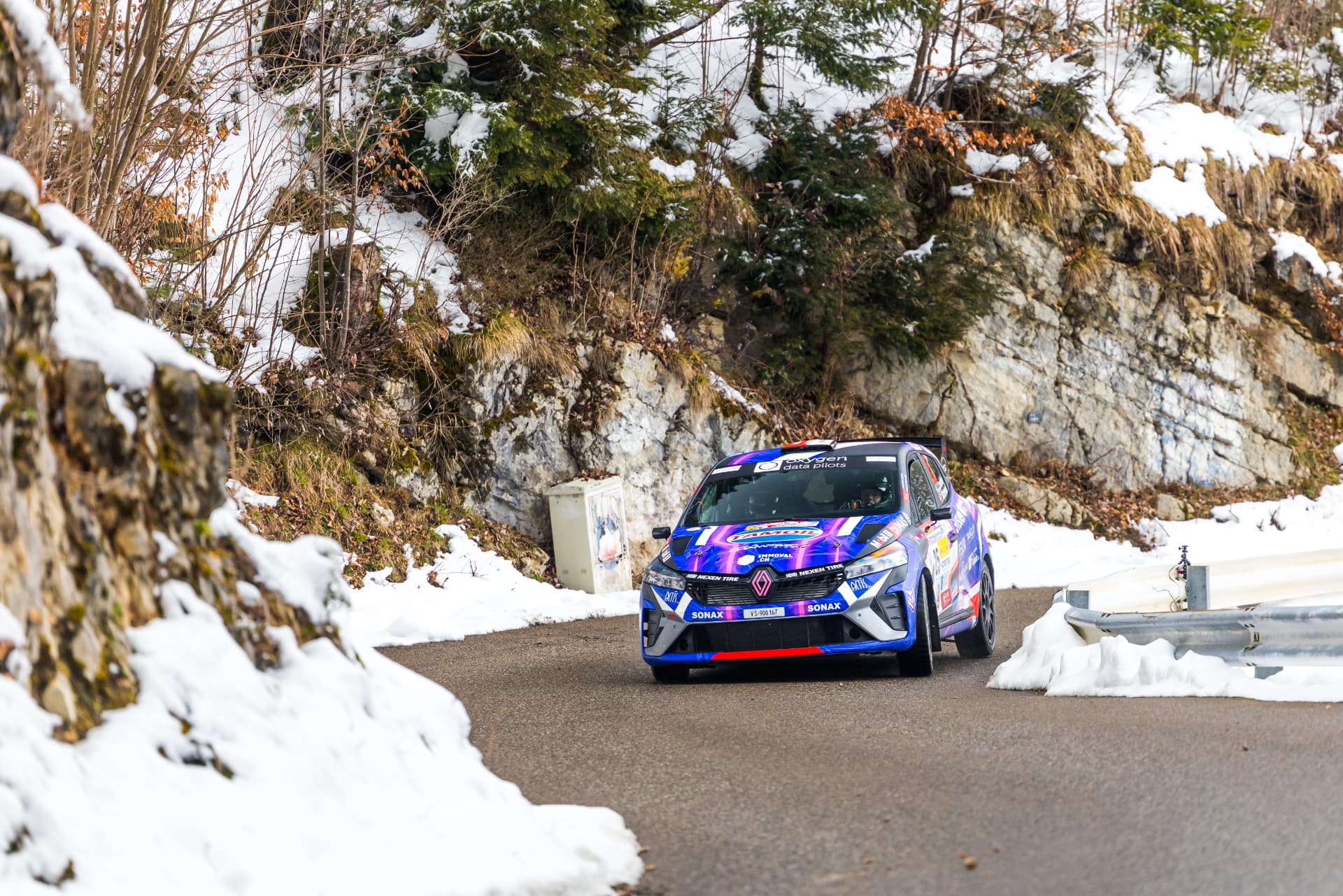 La Clio Rally3 n°25 au pied d'une paroi rocheuse enneigée du Critérium Jurassien