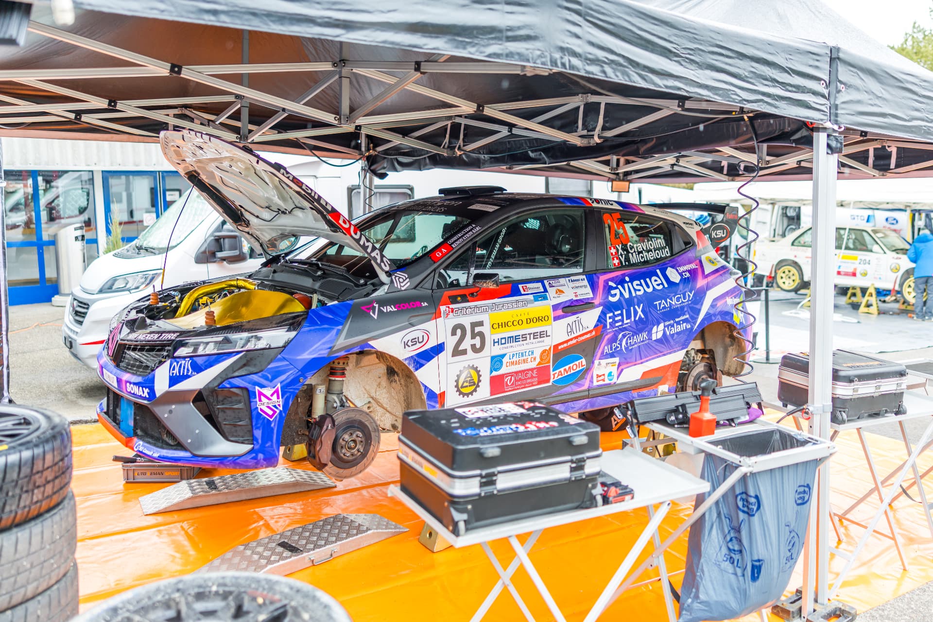 La Clio Rally3 n°25 sur chandelles au parc d'assistance, capot ouvert