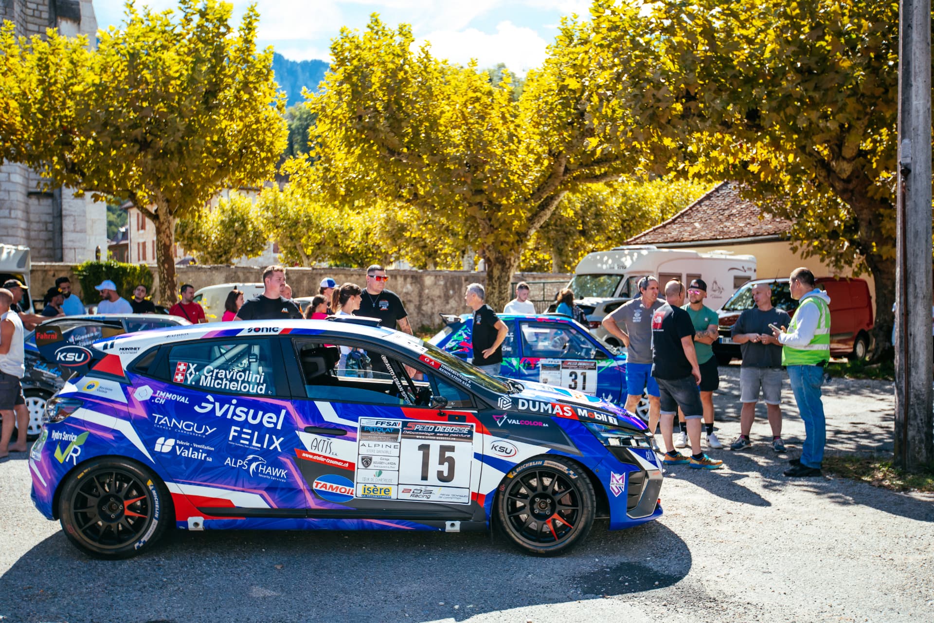 Profil de la Clio Rally3 n°15 sous les platanes, livrée et partenaires visibles