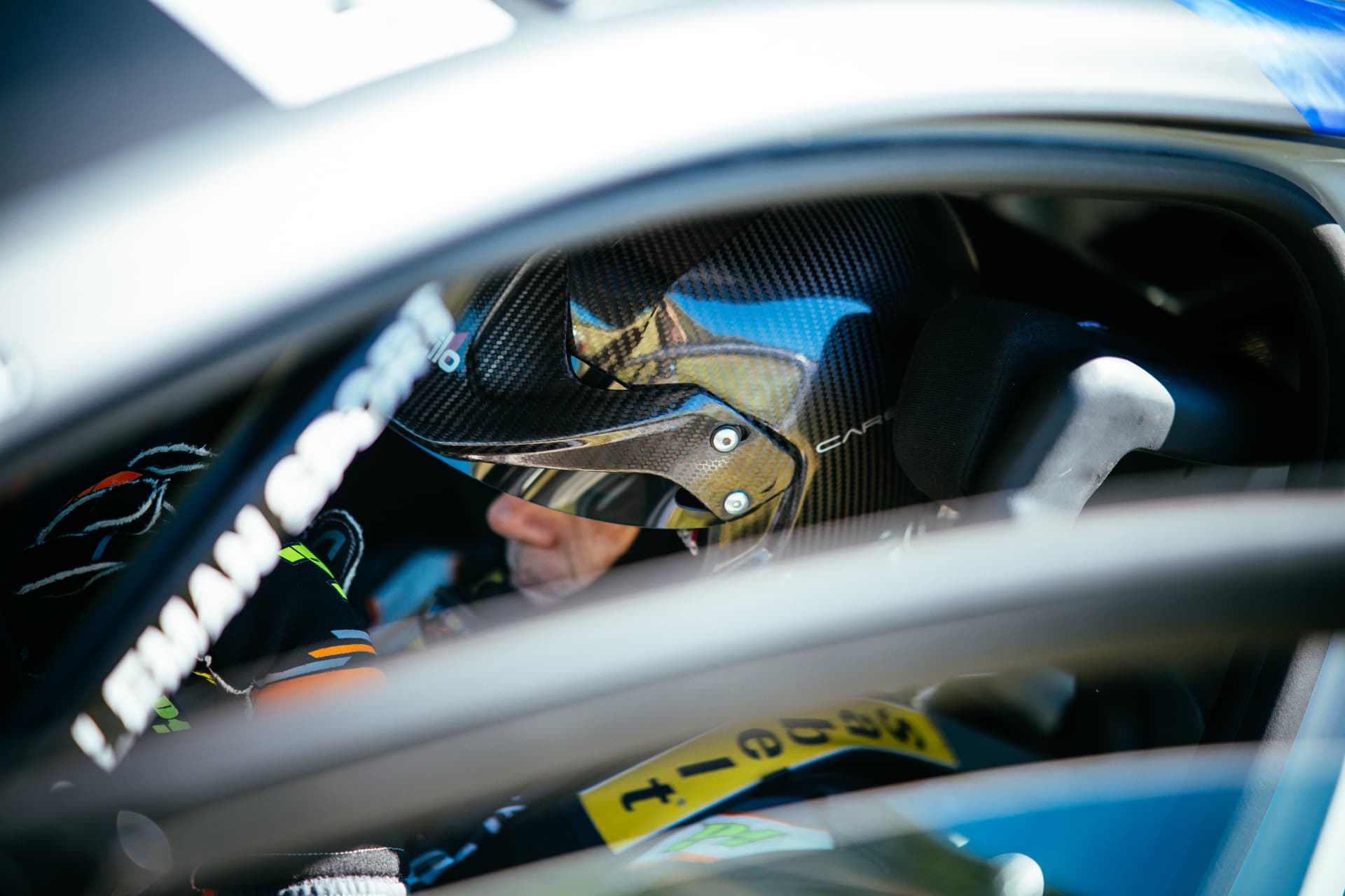 Casque carbone du pilote aperçu à travers la vitre de la Clio Rally3